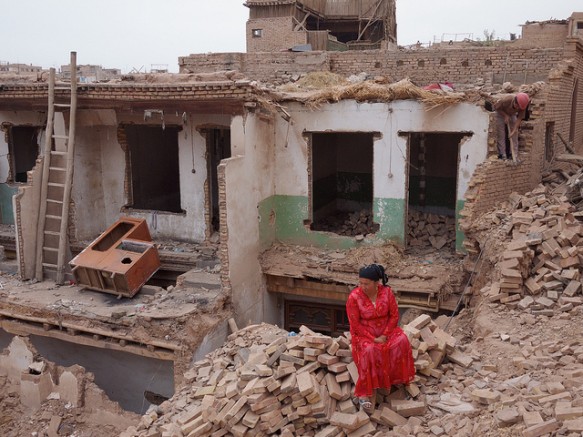 A woman sits on the rubble of her Old City home in Kashgar, Xinjiang